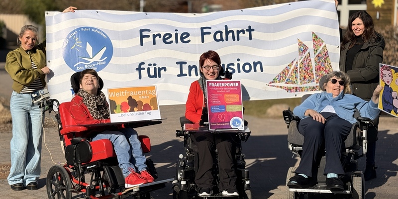 Gruppe von Menschen, darunter zwei im Rollstuhl, vor einem Banner mit der Aufschrift 'Freie Fahrt für Inklusion'